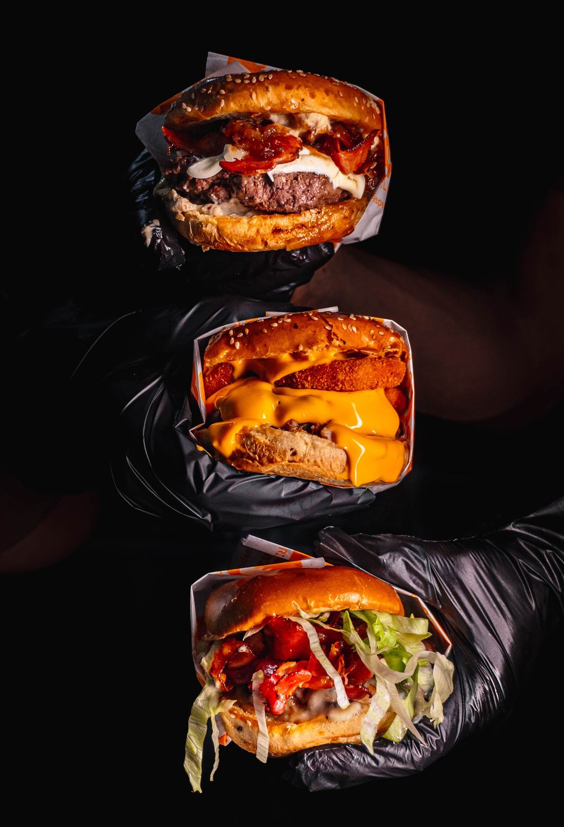 Stacked burgers held in black gloves